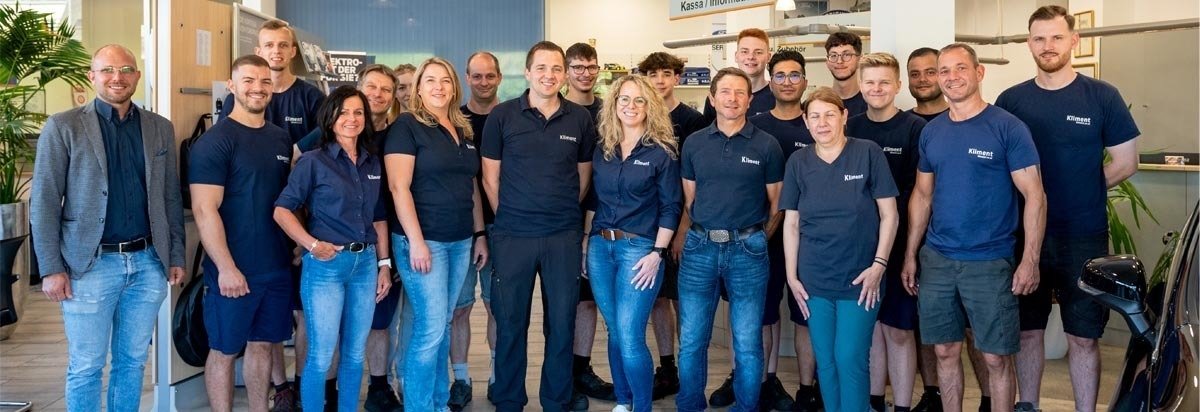 Teamfoto einer Gruppe von Mitarbeitern in Arbeitskleidung, lächelnd in einem modernen Büro, umgeben von Pflanzen.