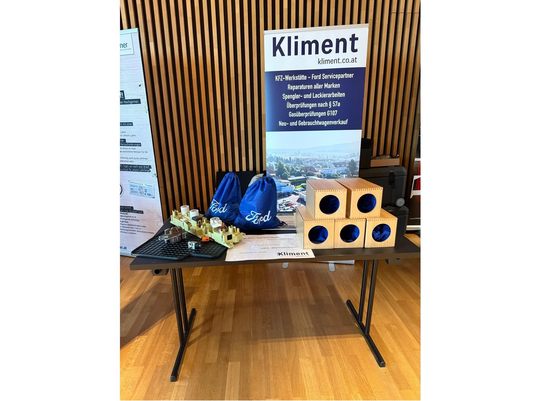 Tisch mit Kliment-Werbefläche, blauen Taschen und Holzboxen bei einer Auto-Service-Veranstaltung.