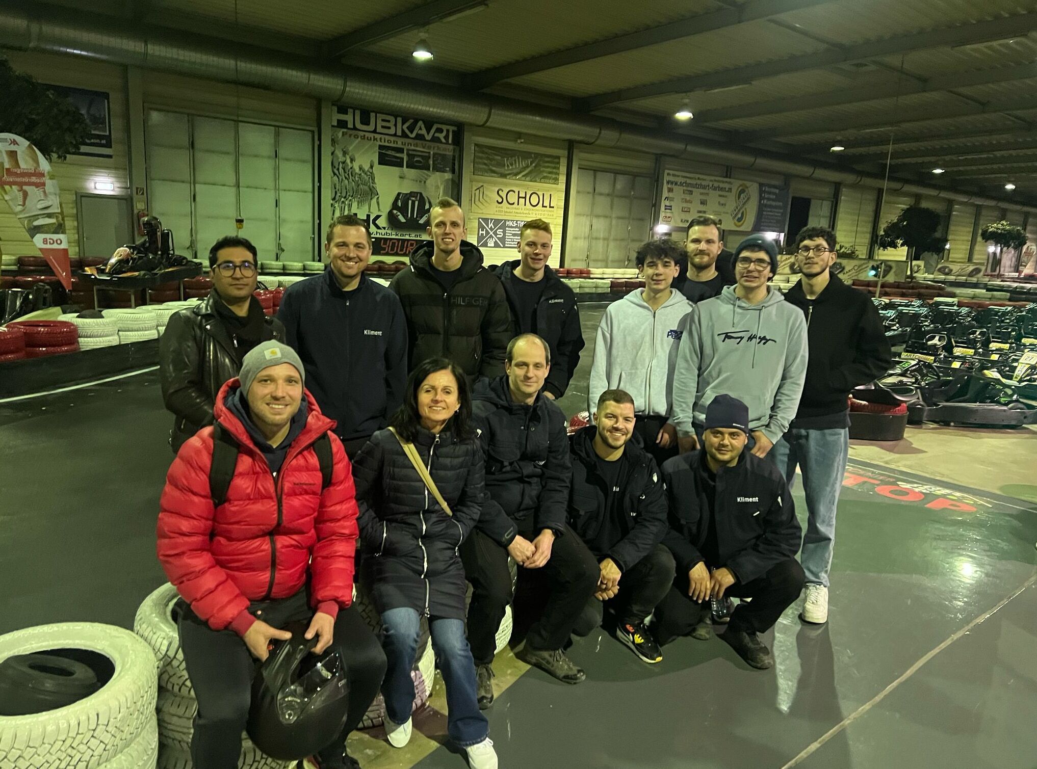 Gruppe von 13 Personen in einer Kartbahn, posierend für ein Foto mit Karts im Hintergrund.