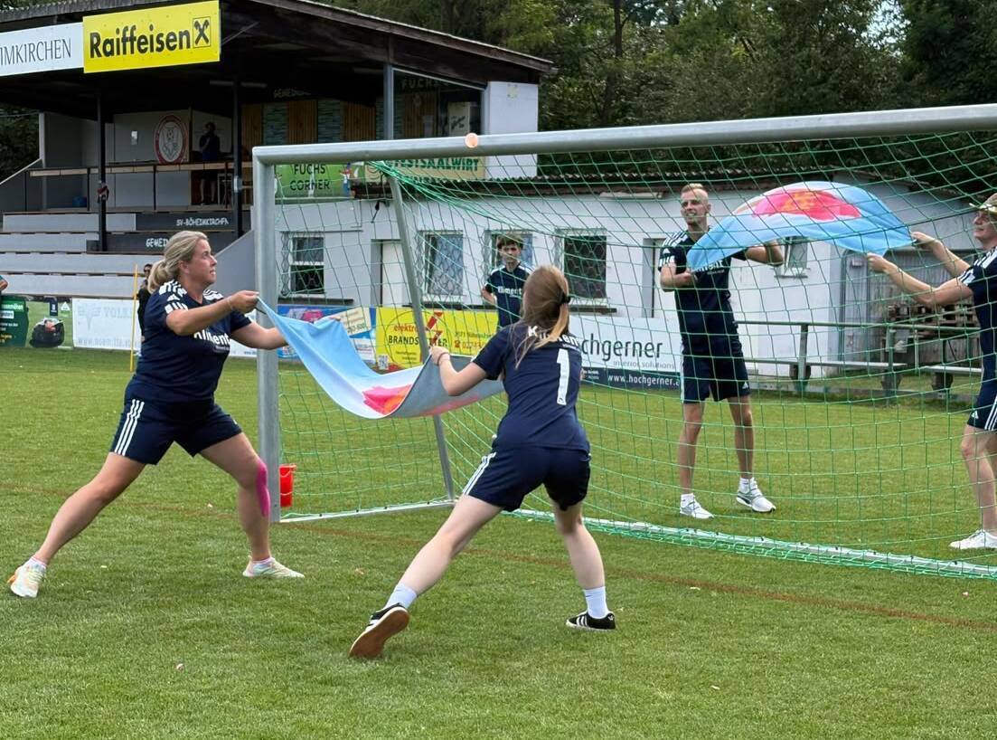Drei Spieler halten Fahnen und werfen sie über ein Fußballtor auf einem Sportplatz.